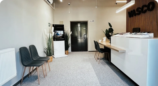 Nowoczesny, biały biurowiec z pionowymi czarnymi pasami i wyposażeniem dachu, otoczony zielenią i drogami, widziany z góry. Z przodu widnieje napis V.AFI EUROPE .