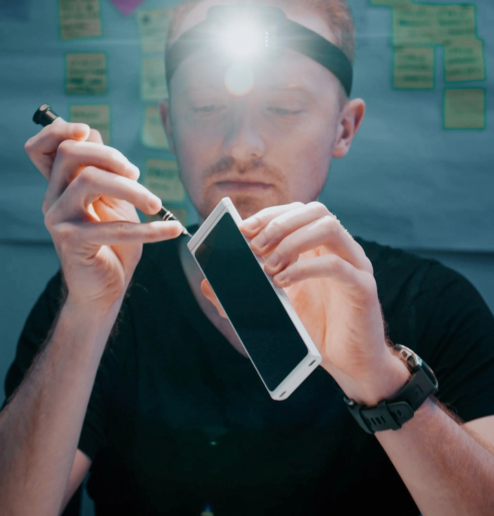 Osoba nosząca czołówkę używa małego śrubokręta do złożenia tłumacza, a w tle na ścianie widoczne są karteczki samoprzylepne.