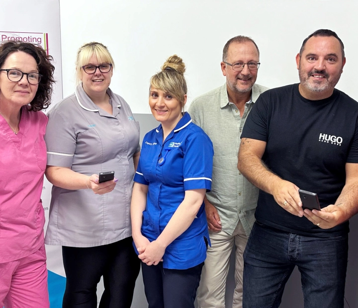 Pięć uśmiechniętych osób stoi razem w strojach medycznych, a dwie z nich trzymają urządzenie tłumaczące.