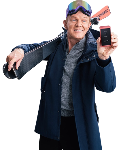 Cezary Pazura stojący za prezentami, w zimowym swetrze, trzyma w rękach pudełko z Vasco Translatorem.