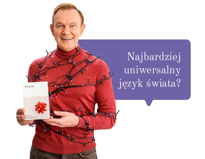 Uśmiechnięty Cezary Pazura w czerwonym swetrze, owinięty lampkami, trzyma w ręce pudełko Vasco Translatora. W tle dymek z tekstem: Najbardziej uniwersalny język świata?