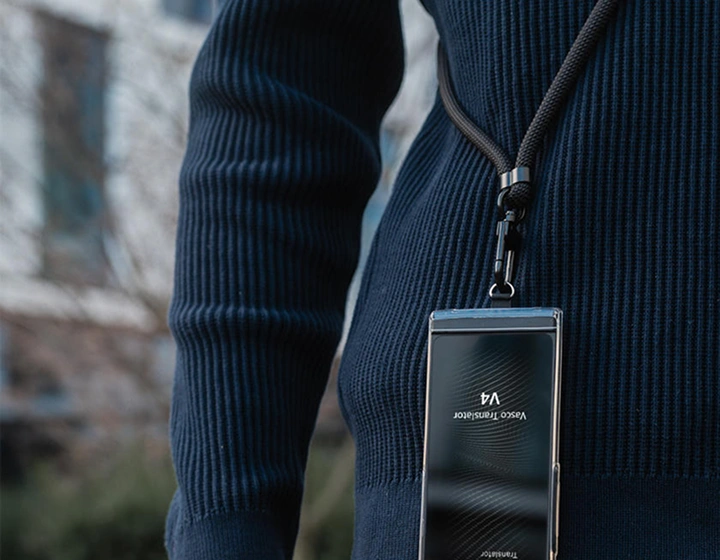 Osoba ubrana w granatowy sweter z czarną smyczą Vasco przymocowaną do Vasco Translator V4; urządzenie jest w kolorze niebieskim.