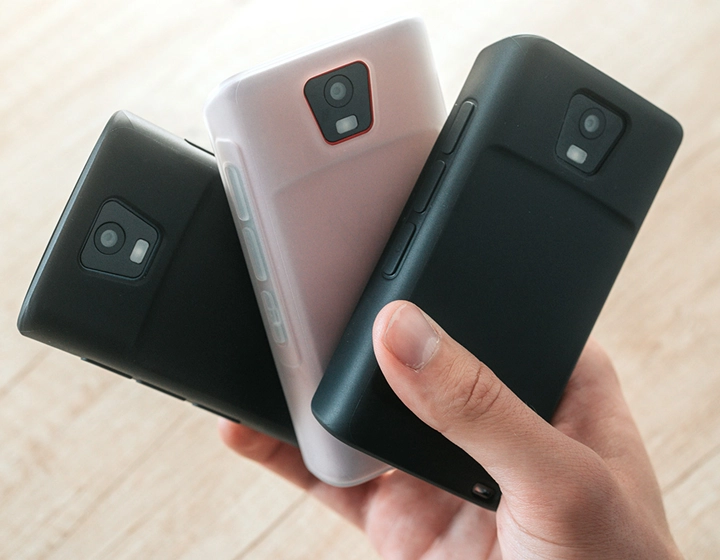 Osoba trzymająca trzy urządzenia Vasco Translator Q1 w silikonowych etui. Etui są w trzech różnych kolorach: jednolitym czarnym, ciemnokarmelowym i mlecznobiałym.